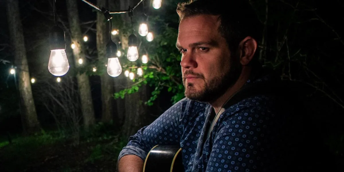 Benny Bassett holding a guitar outdoors under string lights at night