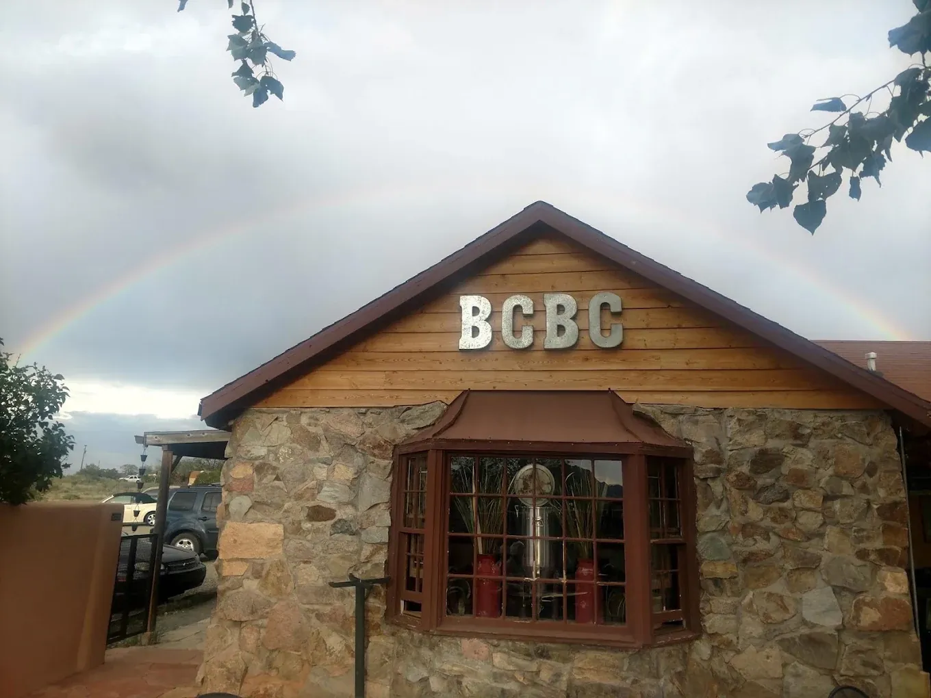 Exterior of Beer Creek Brewing Company near Santa Fe, with the stone-and-wood building, BCBC sign and a rainbow in the sky.