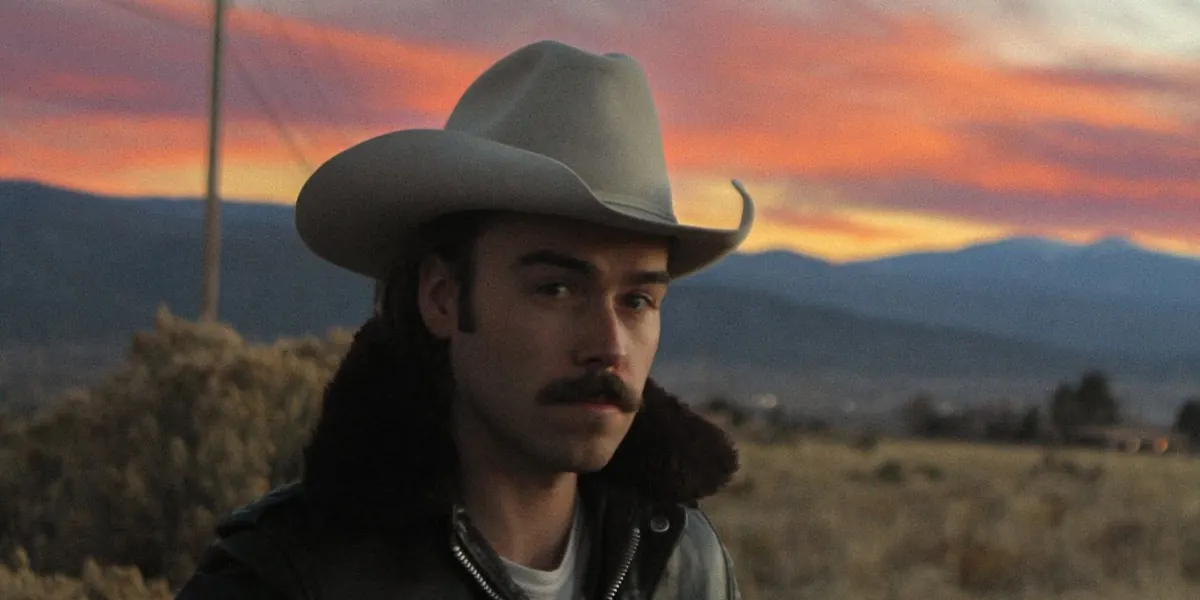 Santa Fe musician Grant Knoxlyn wearing a cowboy hat against a mountain sunset.