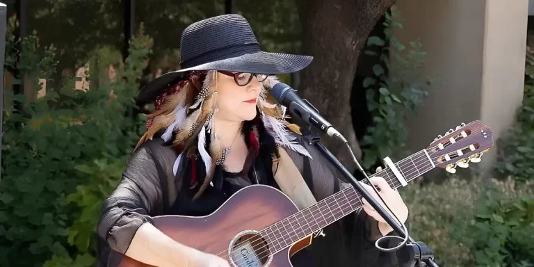 Jennifer Savage Hurley performs outdoors with an acoustic guitar and microphone.